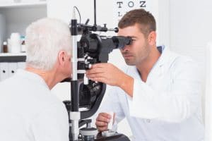 Male optometrist examining senior mans eyes through slit lamp in clinic